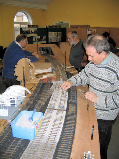 Ballasting of the track between the platforms is nearing completion, cardboard placholders of the station buildings are still in place